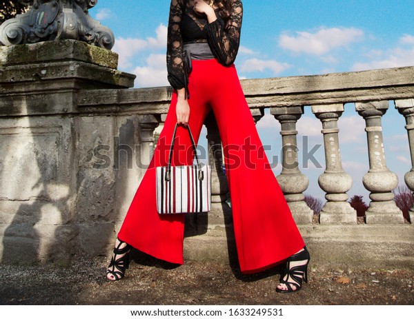Woman with red wide pants holding the\
handbag purse on the bridge. Fashion\
shoot.