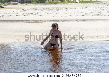 A woman is in the reddish water of the Guaibimzinho River. Praia do Guaibim, coast of the sea of Bahia, Brazil