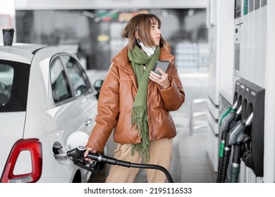 Woman refueling car with gasoline, using smartphone to pay. Concept of mobile technology for fast refueling without visiting the store
