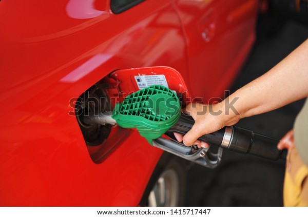 A woman refueling with the gun of hose\
the fuel tank red car  at the gas station,\
Spain