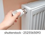 Woman regulates temperature at home with the heating knob on room battery. Metal radiator with individual control. heating system, energy crisis, energy saving, heat saving, heating season