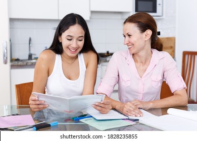 Woman rejoicing at good marks of her teenage daughter in kitchen