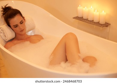 Woman, relax and bath with candles in home for body care, selfcare and cleaning routine in bathroom. Girl, person and resting in bathtub with foam, wellness and ambient for pamper, zen and hygiene - Powered by Shutterstock