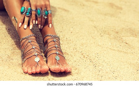 Woman In Relaxation On Tropical Beach with sand , body parts  . Tanned girl leg with silver jewelry,bracelets and rings with turquoise.Boho style feet and hands