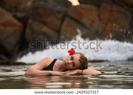Woman relaxes in serene rock-lined lagoon, red flower adorns hair, tranquil swim in natural pool. Solo traveler enjoys secluded waterscape, reflecting on lifes simplicity amidst natures embrace.