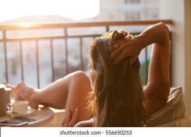 Woman relaxing at balcony enjoying sunrise. Good morning