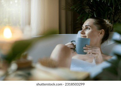 woman relaxing in bath and drink a coffee at home bathroom. looking out of window - Powered by Shutterstock