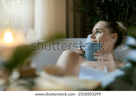 woman relaxing in bath and drink a coffee at home bathroom. looking out of window