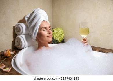 woman relaxing in bath full of foam with glass of champagne in SPA hotel - Powered by Shutterstock