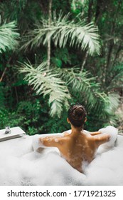 Woman Relaxing In Bath Tub Full Of Foam Outdoors With Jungle View. View From Behind. Unrecognizable Person. Beauty Spa Treatment, Leisure Time.