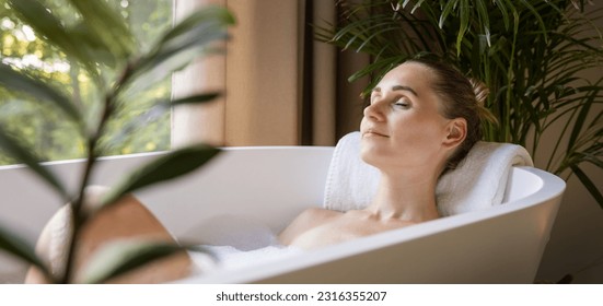 mujer relajante en la bañera con los ojos cerrados en el cuarto de baño con plantas tropicales verdes. tratamiento de spa, cuidado del cuerpo y de la piel. banner con espacio de copia