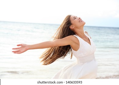 Woman Relaxing At Beach Enjoying Summer Freedom With Open Arms And Hair In The Wind By The Water Seaside. Mixed Race Asian Caucasian Girl On Summer Travel Holidays Vacation Outside.