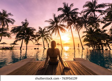 Woman relaxing by the pool in a luxurious beachfront hotel resort at sunset enjoying perfect beach holiday vacation - Shutterstock ID 763956139