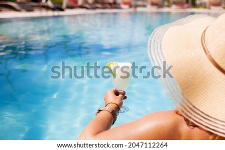 Woman relaxing by poolside and holding glass of cocktail in luxury all-inclusive tropical resort