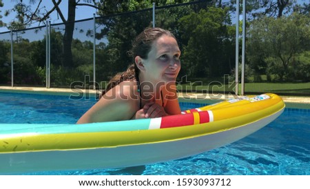 
Woman relaxing by swimming pool holding on inflatable mattress