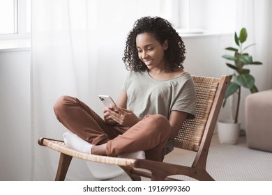 Woman relaxing in chair, using smartphone at home. Student girl looking at mobile phone in her room. Communication, work or study from home, connection, mobile apps, technology, lockdown, lifestyle - Shutterstock ID 1916999360