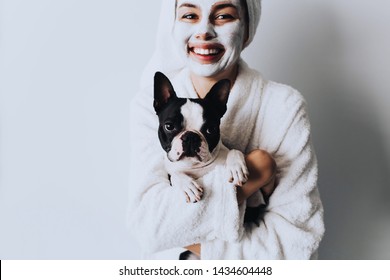 Woman Relaxing With A Charcoal Facial Mask At Home With Her Dog.Beautiful Woman With A Clay Or A Mud Mask On Her Face Over White Background