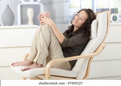 Woman relaxing with closed eyes and cup of tea in armchair at home, daydreaming. - Powered by Shutterstock