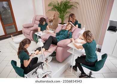Woman relaxing in comfortable salon chair while having manicure, pedicure and eyelash extension procedure. Manicurist, pedicurist and eyelash specialist working with client in modern beauty salon.