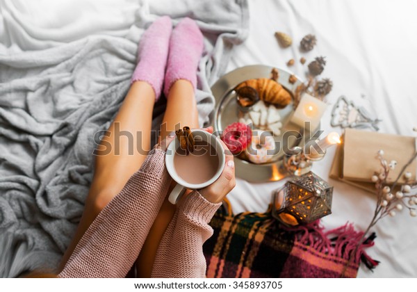Woman relaxing at cozy\
home atmosphere on the bed. Young woman with cup of coffee or cocoa\
in hands and cookies enjoying comfort. Soft light and comfy\
lifestyle concept.