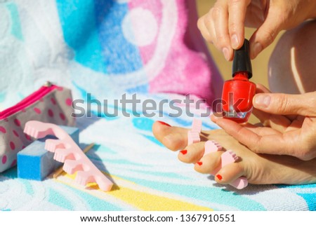 Woman relaxing doing her pedicure with red nail polish on beach towel. Female taking care of feet