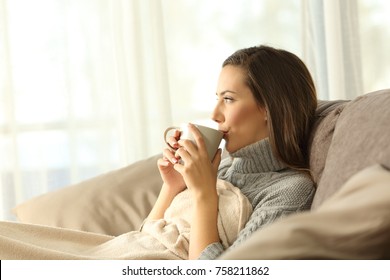 Woman relaxing drinking coffee sitting on a sofa in the living room in a house interior - Powered by Shutterstock