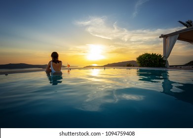 Woman Relaxing At The Edge Of Infinity Swimming Pool At Sunset