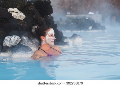 Woman relaxing in geothermal spa in hot spring pool in Iceland. Girl enjoying bathing in a blue water lagoon with famous healing mud on her face.