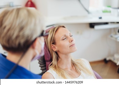 Woman relaxing with her eyes close at the dentist as she sits in the examination chair viewed over the shoulder of the dentist or nurse - Powered by Shutterstock