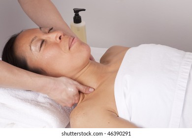 A woman relaxing with her eyes closed while she is getting her neck massaged at the spa.
