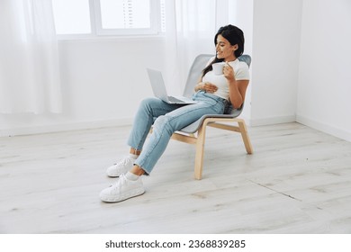 Woman relaxing at home sitting in a chair and watching a movie on her laptop with a cup of tea, happiness and laughter comedy, freelancer lifestyle - Shutterstock ID 2368839285