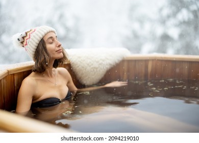 Woman relaxing in hot bath outdoors, enjoying thermal spa at snowy mountains. Winter holidays in the mountains, hot water treatments concept. Caucasian woman wearing winter hat - Shutterstock ID 2094219010