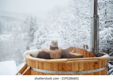 Woman relaxing in hot bath outdoors, sitting back and enjoying beautiful view on snowy mountains. Winter holidays in the mountains, hot water treatments concept. Caucasian woman wearing winter hat - Shutterstock ID 2195286601