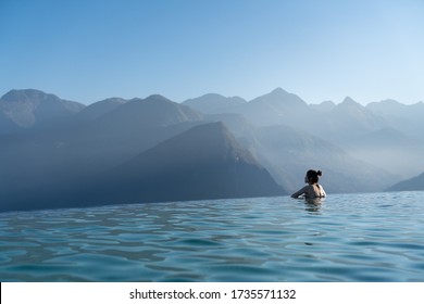 woman relaxing in infinity swimming pool   looking at stunning mountain view at  luxurious resort / vacation concept