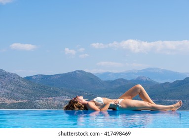 Woman Relaxing In Infinity Swimming Pool Looking At View