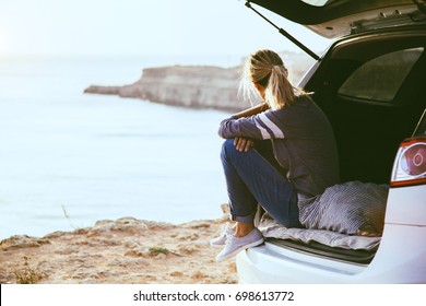 Woman relaxing inside car trunk and watching on sea. Fall trip in sunset. Freedom travel concept. Autumn weekend.