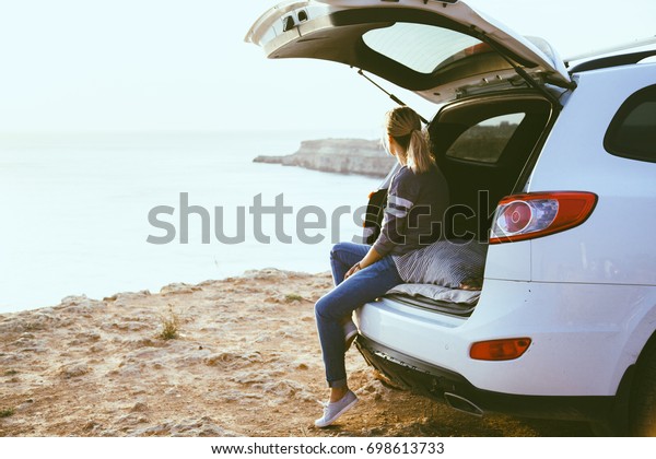 Woman relaxing
inside car trunk and watching on sea. Fall trip in sunset. Freedom
travel concept. Autumn
weekend.