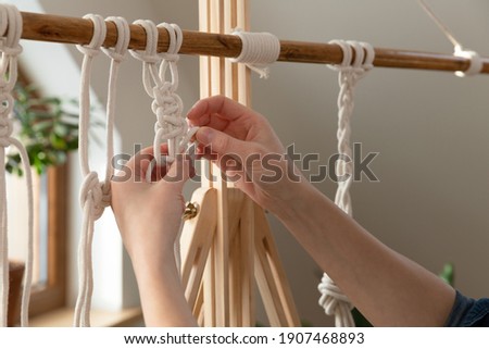 Woman relaxing and making macrame at home with different knots on a sunny day at home in attic. Stay at home hobbies.