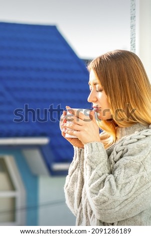 Woman relaxing on the balcony with coffee. A beautiful young woman in a sweater holds a cup of coffee standing near the window in the morning
