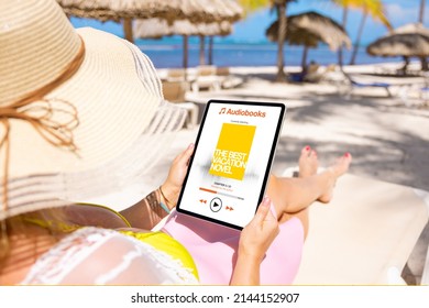 Woman Relaxing On The Beach And Listening To An Audiobook