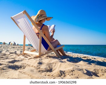 Woman Relaxing On Beach Reading Book Sitting On Sunbed