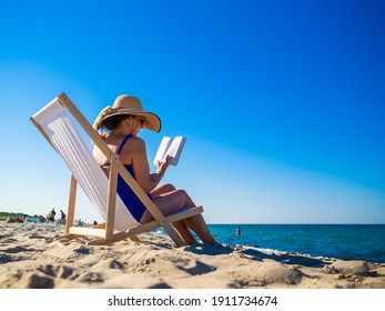 Woman relaxing on beach reading book sitting on sunbed 