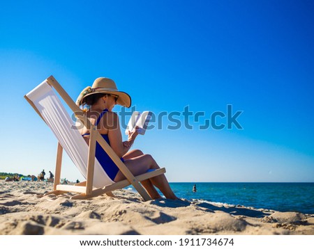 Woman relaxing on beach reading book sitting on sunbed 