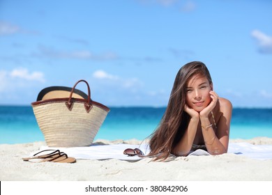 Woman Relaxing On Beach Vacation Summer Holidays. Beautiful Asian Girl Lying Down On Towel With Straw Hat And Flips Flops On White Sand Tanning. Sun Hair And Skin Care Concept.