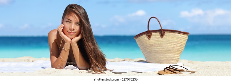 Woman Relaxing On Beach Vacation Summer Holidays Banner With On Sky And Blue Ocean. Beautiful Asian Girl Lying Down On Towel With Flips Flops And Beach Bag Tanning. Sun Hair And Skin Care Concept.