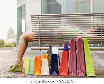 Woman Relaxing On Bench Outside Shopping Center. Horizontal Shape, Full Length