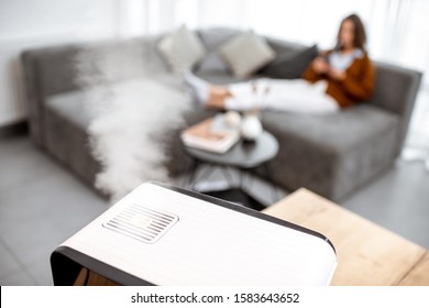 Woman relaxing on the couch at home with working air humidifier on the foreground. Concept of home air humidification during a winter