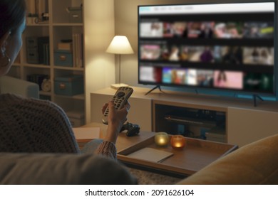 Woman Relaxing On The Couch, She Is Using The Remote Control And Choosing A TV Show Or Movie On The Television Menu