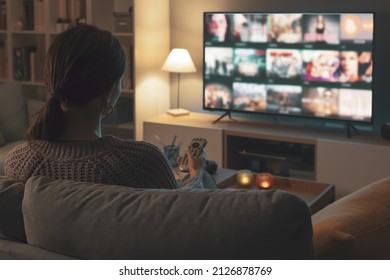 Mujer relajándose en el sofá, está usando el mando a distancia y eligiendo un programa de televisión o una película en el menú de la televisión
