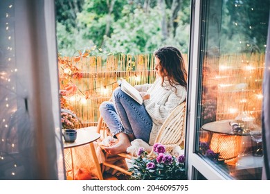 Woman relaxing on cozy balcony, reading a book.  - Shutterstock ID 2046095795